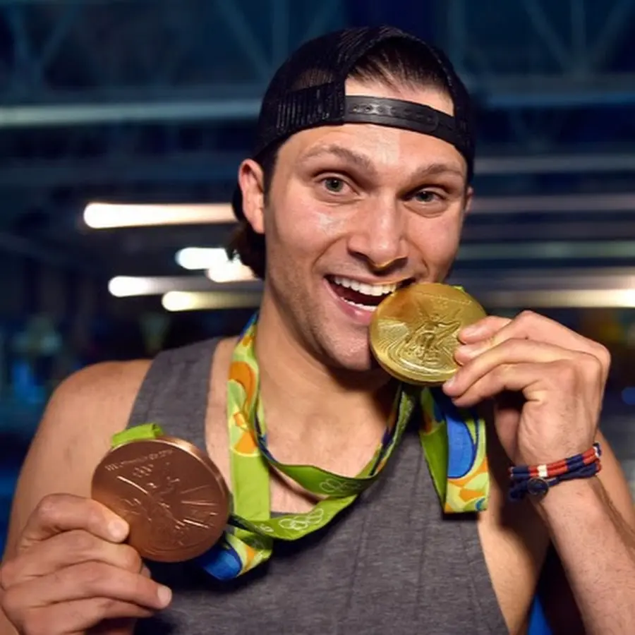 Asea Healing Tao Australia. Cody Miller wearing a black snapback hat and chewing on a gold medal with his teeth after winning the Olympics for Mens Swimming
